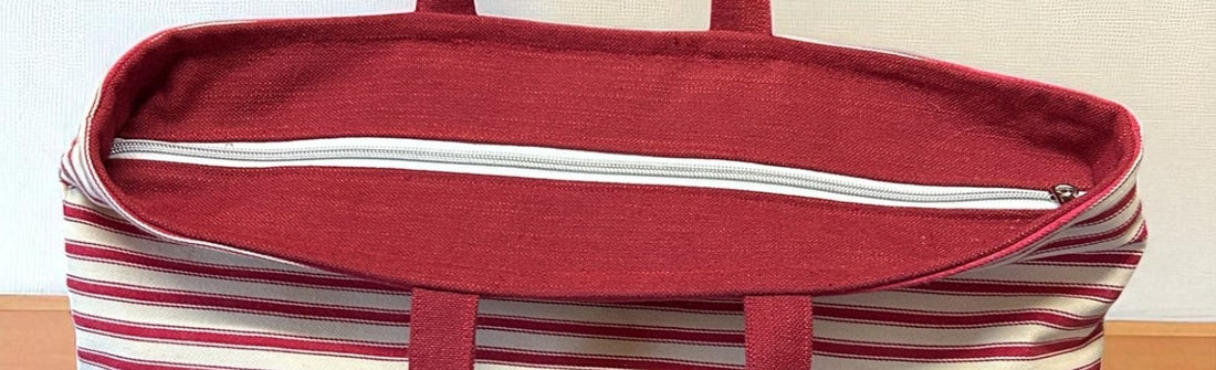 Close-up of a red and cream striped tote bag with a fully closed white zip along the top panel, showing neat stitching and a flat, structured finish.