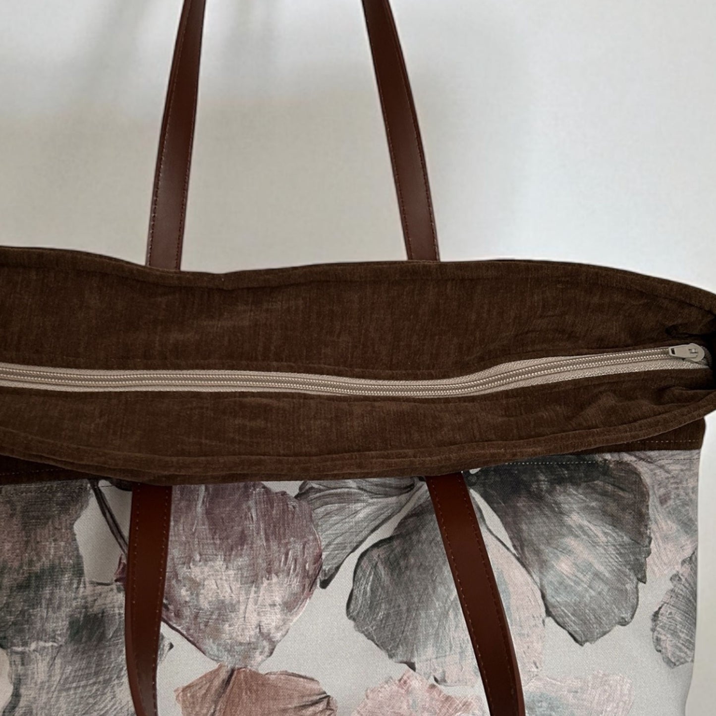 Brown tote bag with floral pattern on a white background, showing zip top