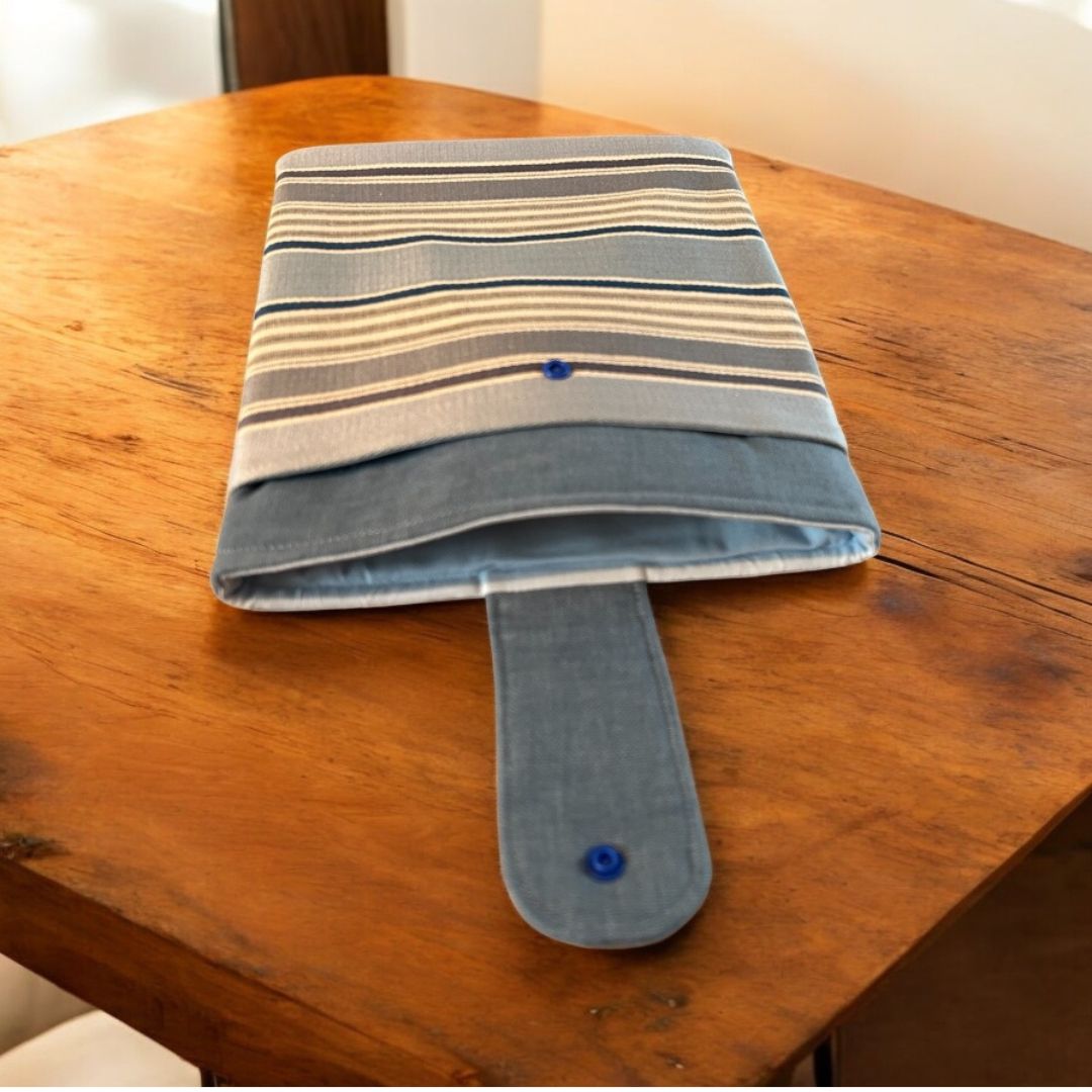 Blue, grey, and beige striped tablet sleeve with front pocket and snap closure, shown open on a wooden table with visible padded interior