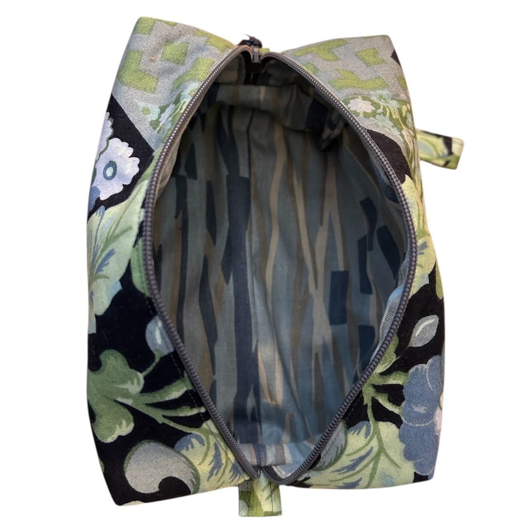 Top-down view of handmade floral makeup bag showing striped cotton lining and open zip, with outer fabric in vintage blue and green floral print.