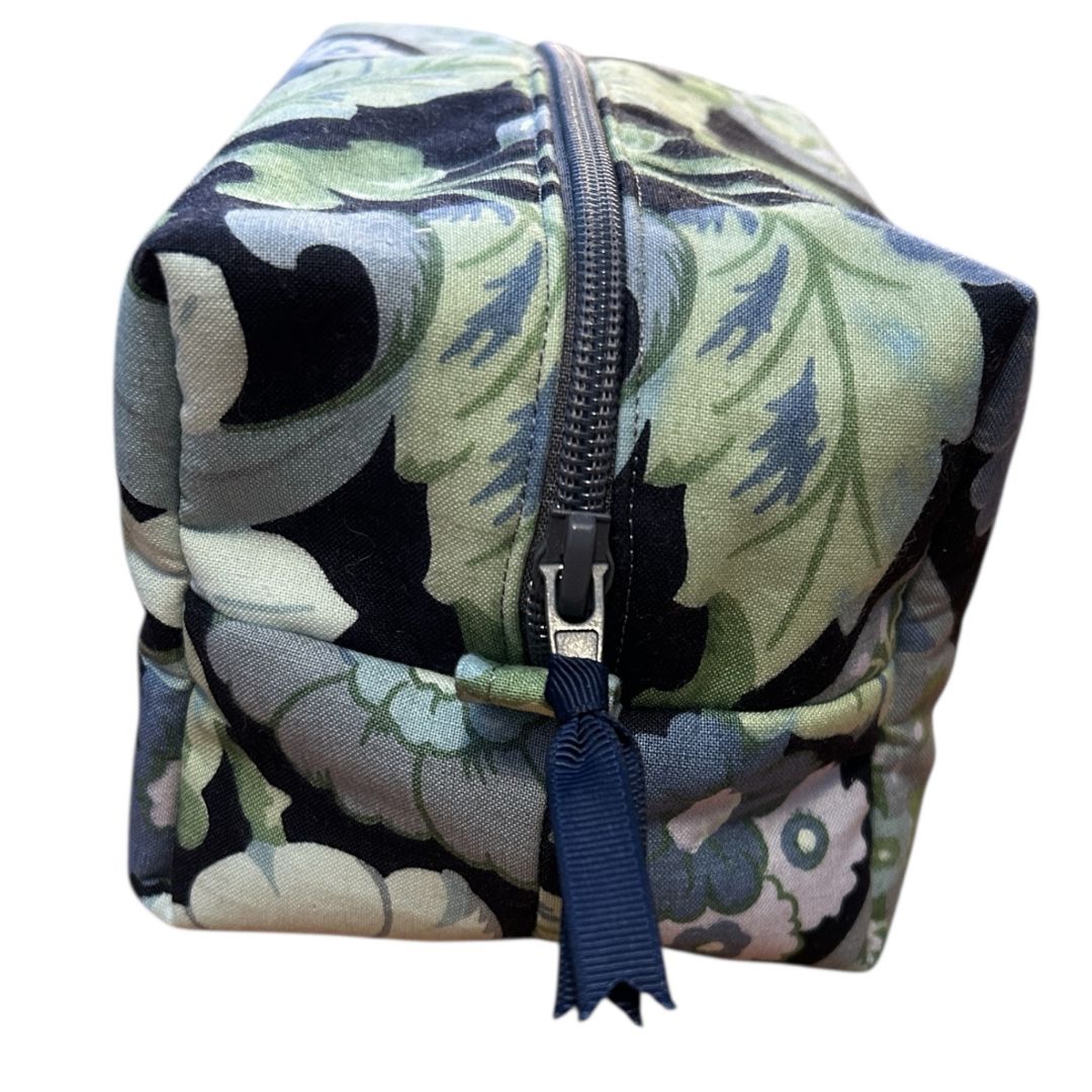 Close-up of handmade makeup bag in vintage blue and green floral fabric, showing boxed corner construction and black zip with navy fabric pull.