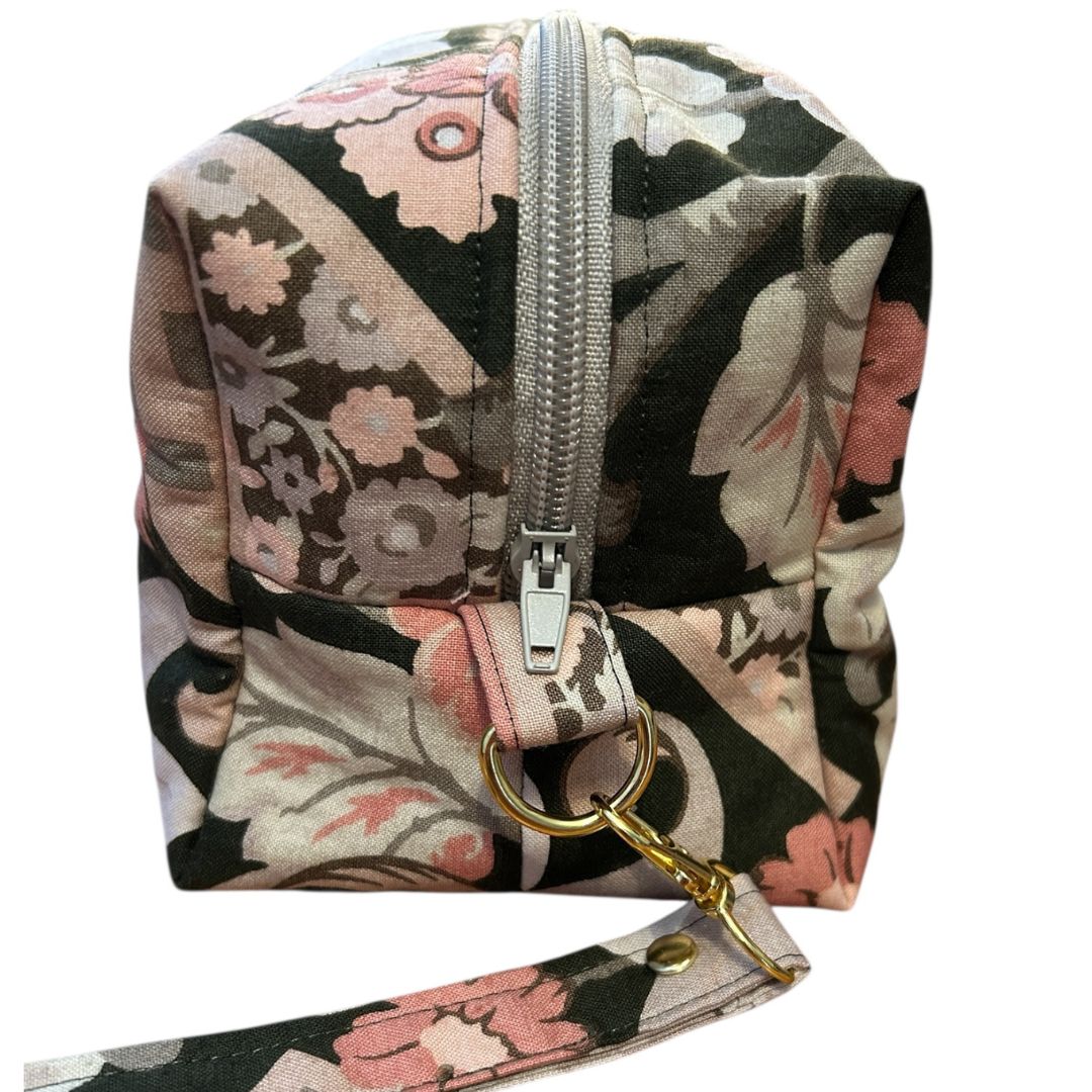 Close-up of a handmade brown floral makeup bag showing silver zip, boxed corner, and detachable wrist strap with gold swivel clasp.