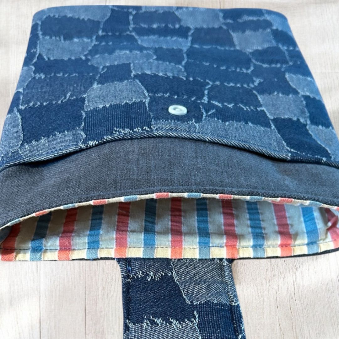 Inside view of a denim patchwork tablet sleeve, showing colourful striped lining and open front pocket on a wooden surface.