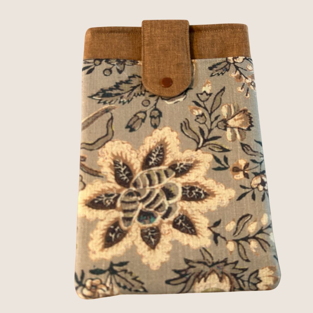 Floral tablet sleeve in taupe, ginger, and cream tones with a snap closure and front pocket, featuring a bold stitched flower design on repurposed fabric