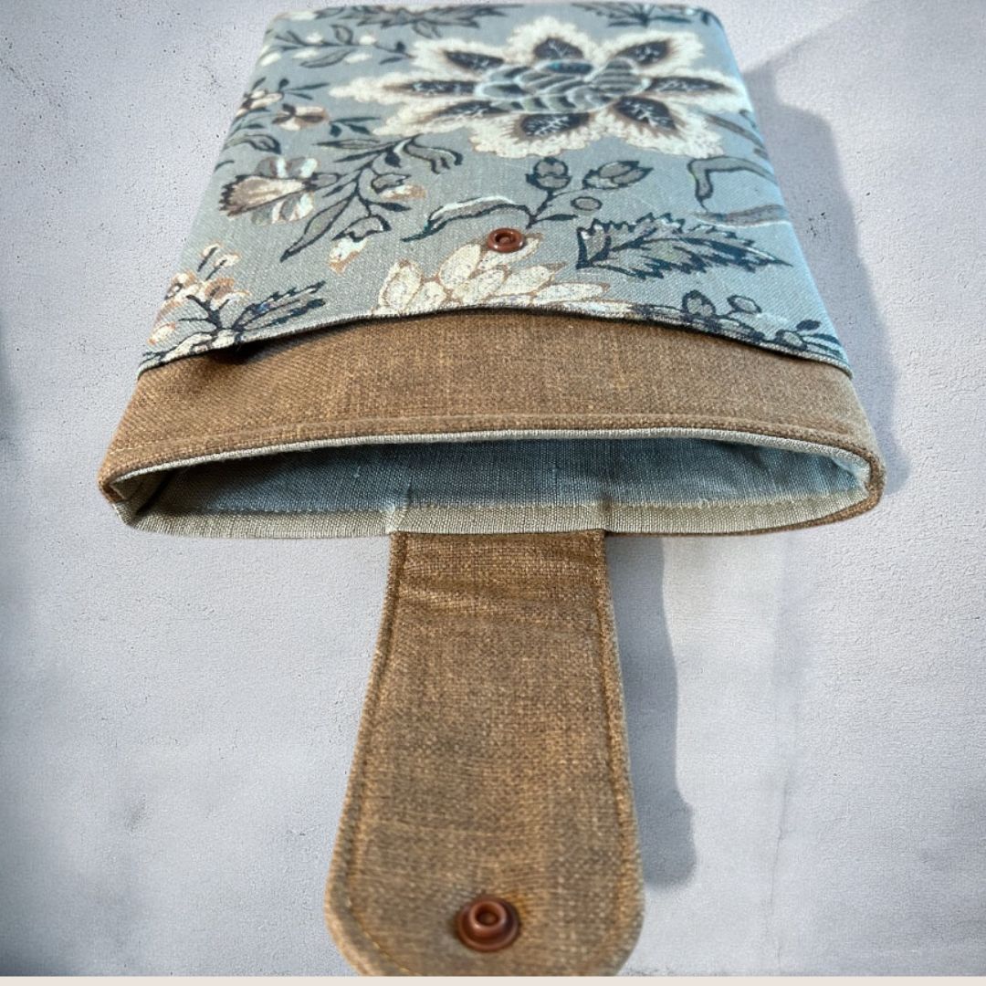 Open view of a taupe and floral tablet sleeve showing the front pocket, soft padded interior, and snap closure tab, displayed against a concrete background