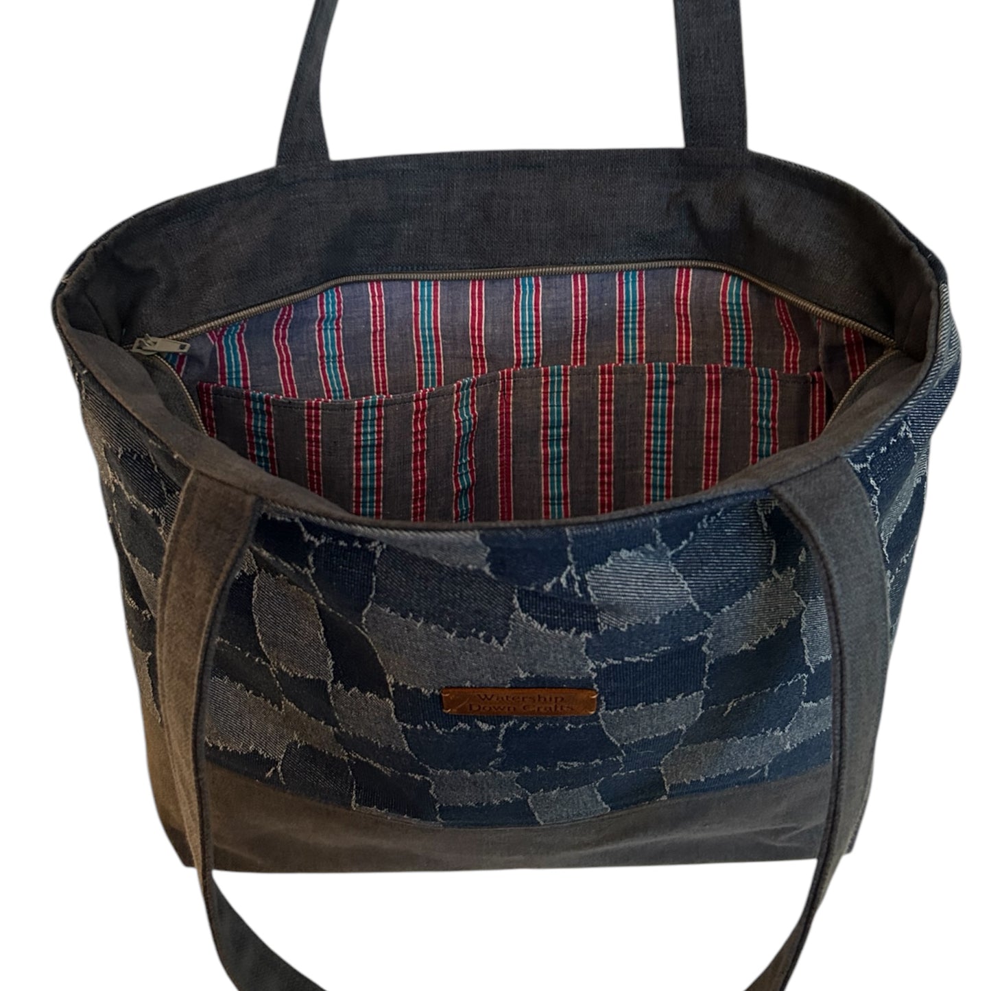 Open denim patchwork tote bag showcasing a vibrant striped interior lining with a spacious pocket for organized storage. The exterior features a handmade checkerboard design and a leather 'Watership Down Crafts' logo tag, combining practicality with artisanal charm