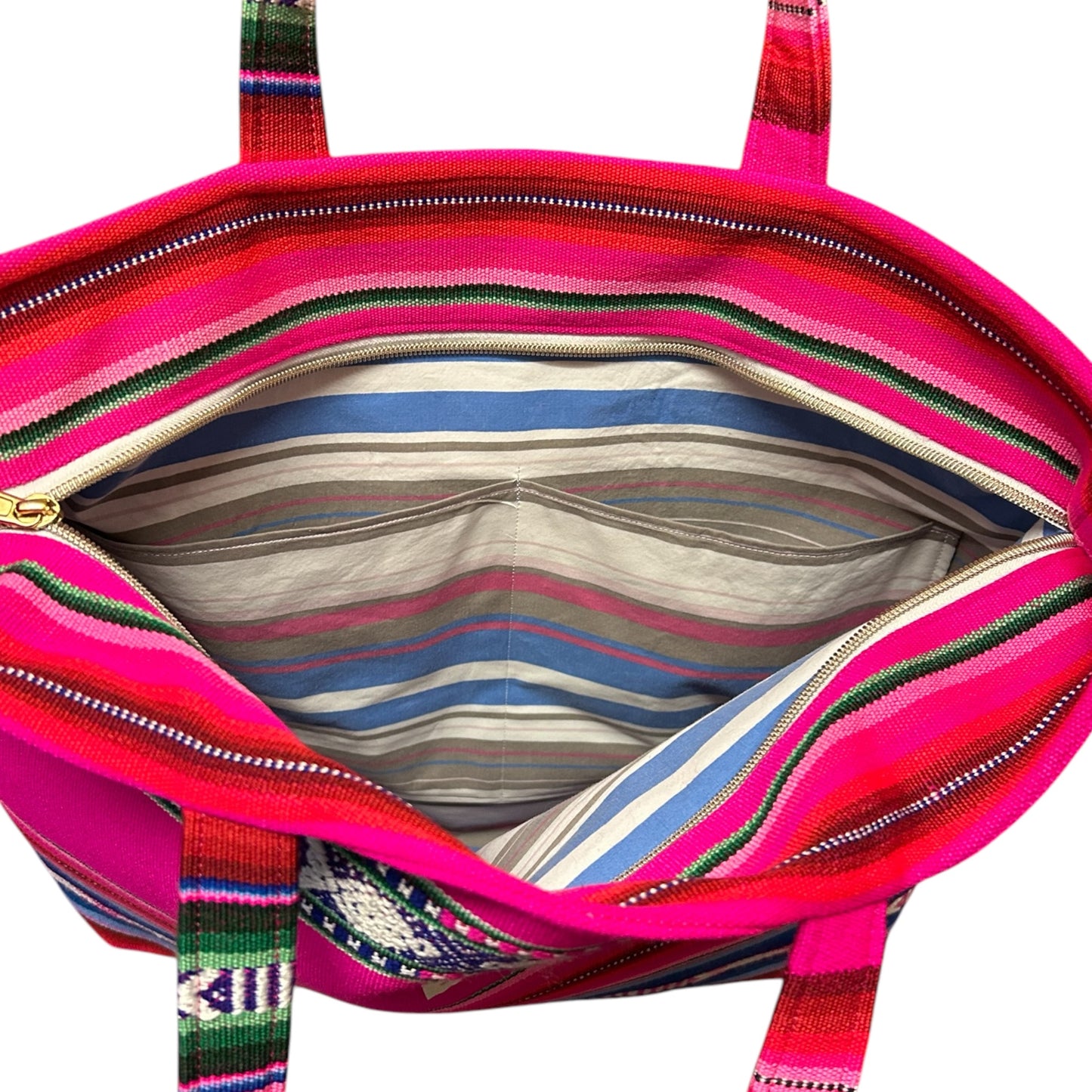 Interior view of a handmade boho tote bag featuring a vibrant striped cotton lining, two slip pockets for organization, and a secure gold inset zipper closure. The bold pink, blue, and green woven fabric adds a stylish and functional touch to this unique design.