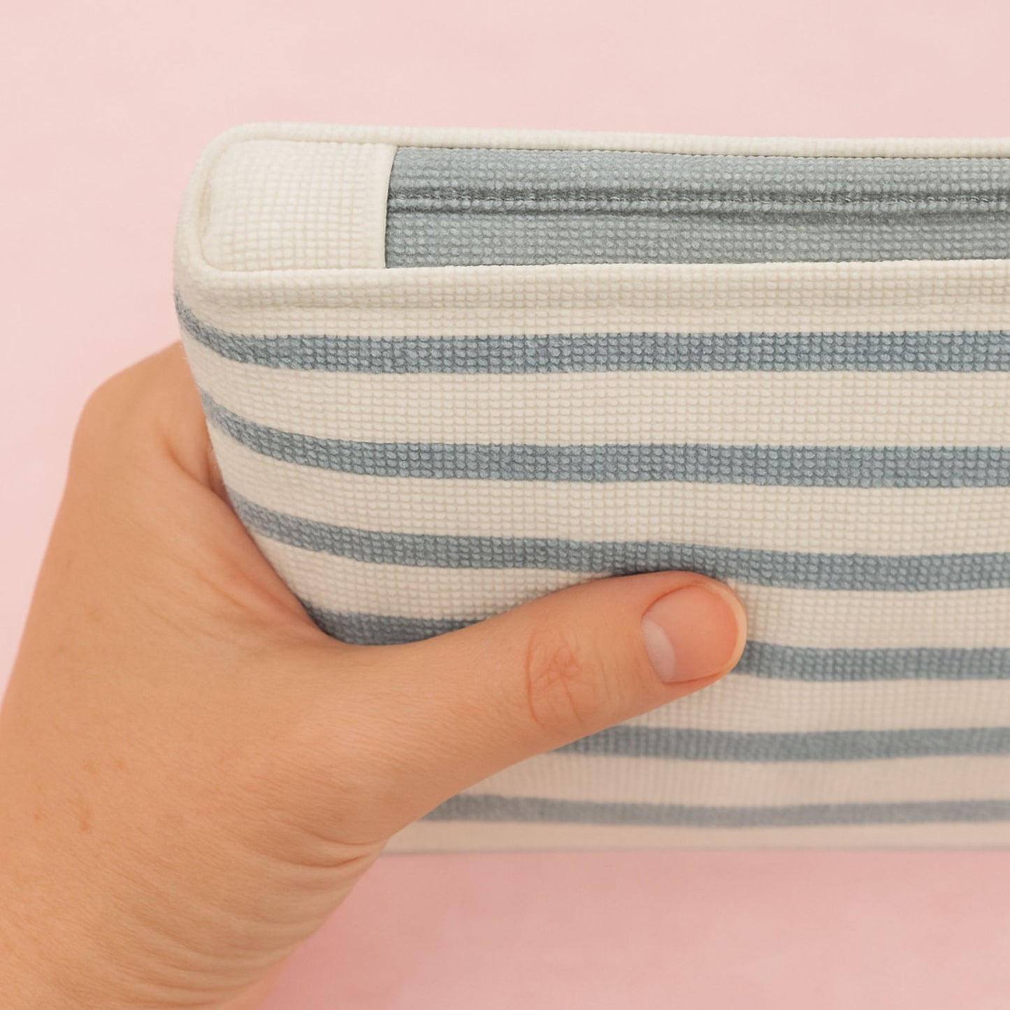Hand holding a striped fabric pouch against a pink background