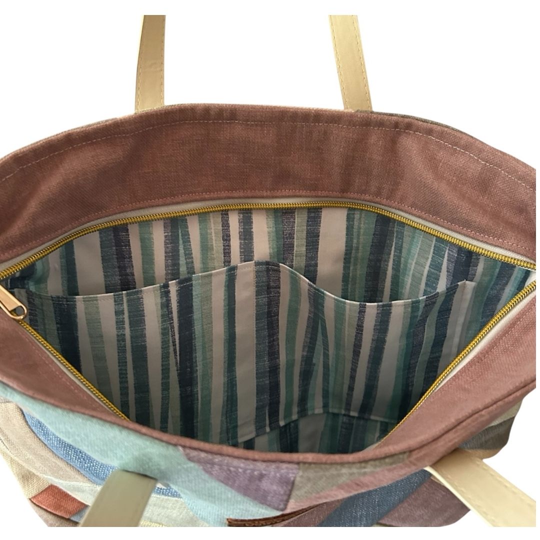 Interior of a pastel patchwork tote bag showing striped cotton lining, two slip pockets, and a zip-top closure.