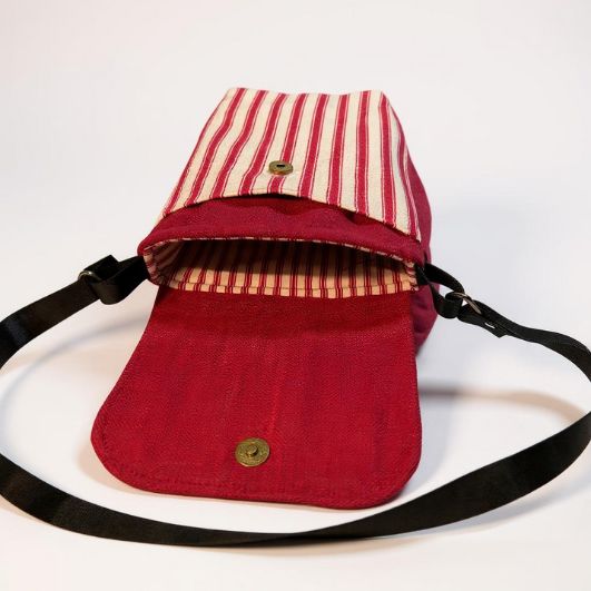 Interior view of a red and cream striped crossbody bag with the magnetic flap open, showing matching striped cotton lining and black adjustable strap.