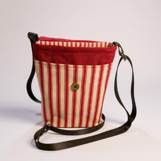 Front view of the crossbody bag showing the striped fabric, snap-fastened external pocket, and black adjustable strap.