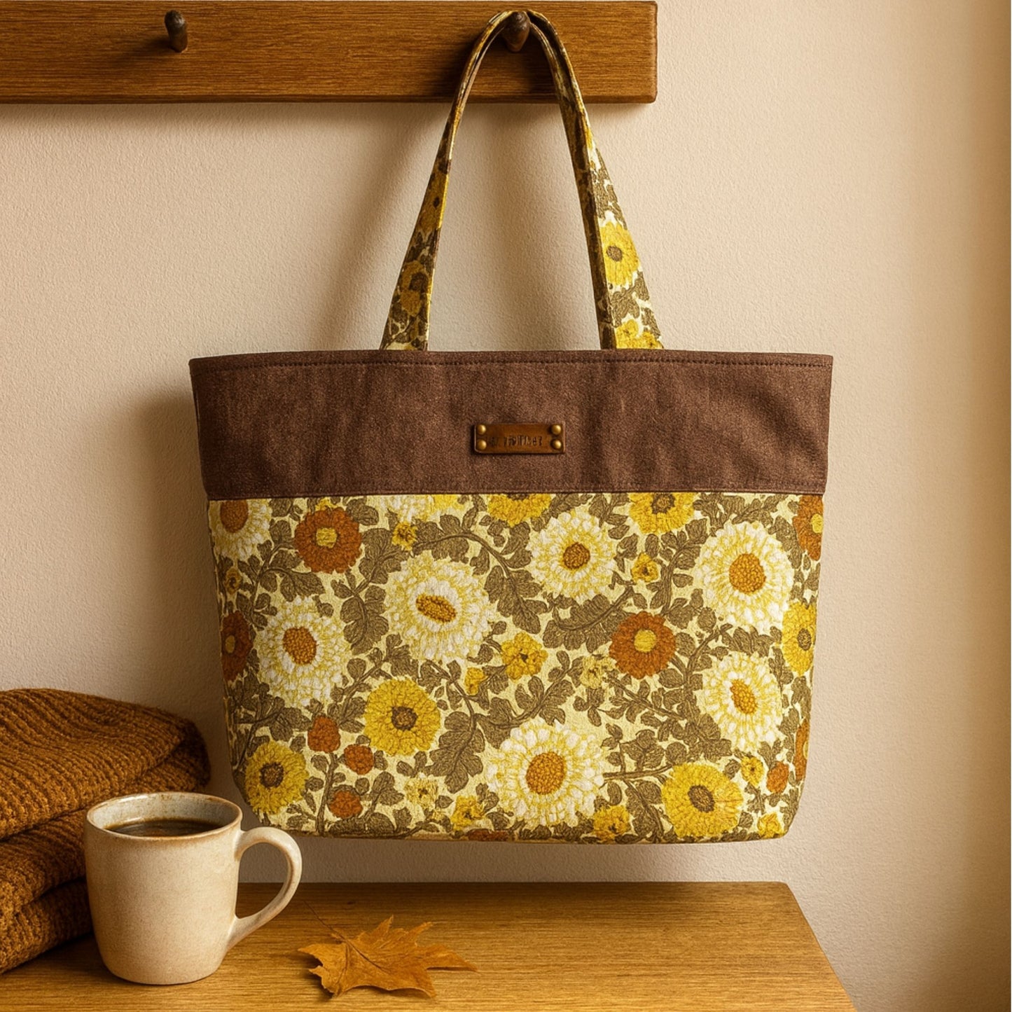 Floral-patterned tote bag with brown top section on a wooden surface next to a mug and blanket.