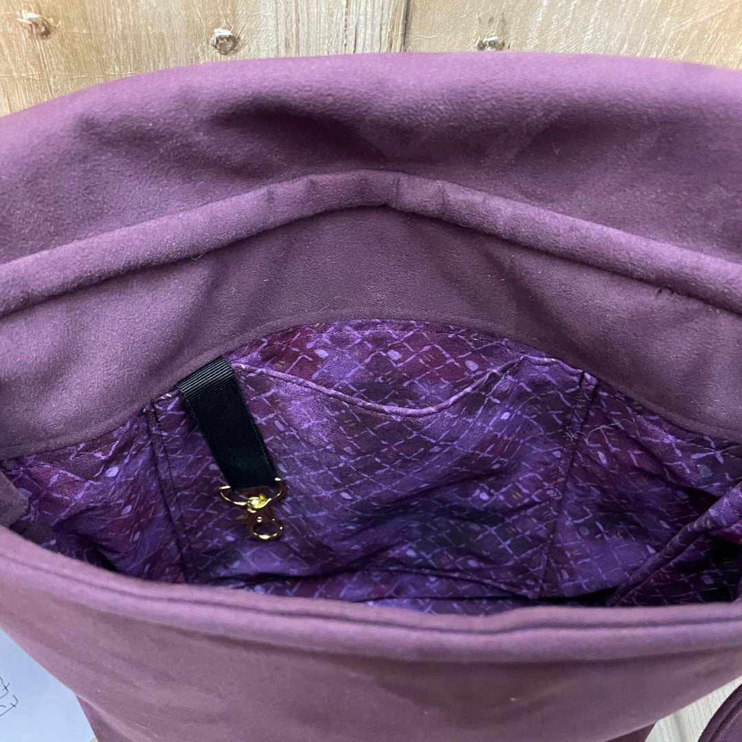 A close-up view of the interior of a maroon shoulder bag, showing the lining and pockets. The lining has a rich purple color with a subtle diamond-patterned texture, adding a decorative touch to the inside of the bag. A small black fabric loop with a gold clasp is attached inside, ideal for securing keys or small items. The soft outer fabric and well-finished inner details highlight the craftsmanship and thoughtful design of the bag.