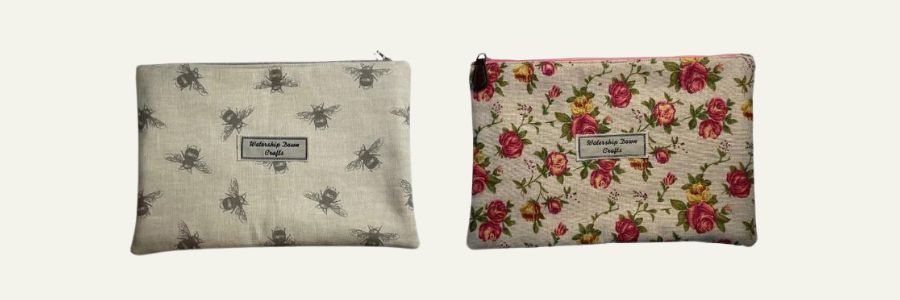 Two handmade zipper pouches side by side, featuring bee-print fabric on the left and floral-print fabric on the right, both with 'Watership Down Crafts' labels, displayed on a neutral background.