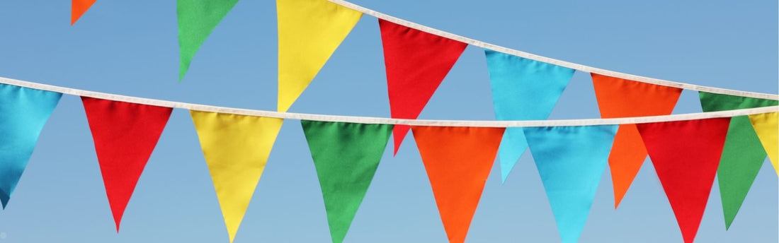 Colourful outdoor bunting with bright red, yellow, green, orange and blue fabric flags hanging against a clear blue sky.