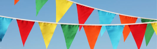 Colourful outdoor bunting with bright red, yellow, green, orange and blue fabric flags hanging against a clear blue sky.