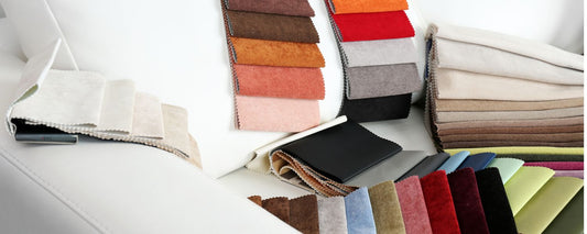 An assortment of colorful fabric swatches, ranging from neutral tones to vibrant reds and greens, displayed on a white sofa, showcasing various textures and materials