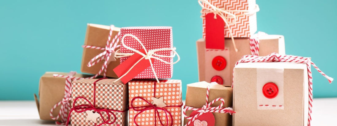 Beautifully wrapped handmade gifts in brown paper with red and white ribbons, buttons, and decorative patterns, stacked against a teal background.
