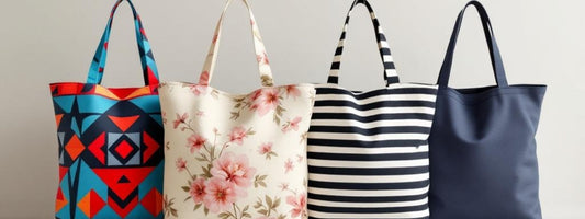 A row of four tote bags in different designs: a bold geometric pattern in red, orange, blue, and black; a cream bag with soft pink floral print; a black and white horizontal stripe design; and a plain navy tote with clean lines.
