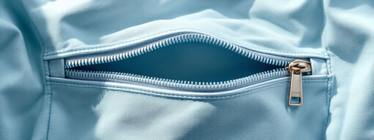 Close-up view of a light blue fabric with a neatly sewn zipper pocket, showcasing the stitching details and a silver zipper pull.