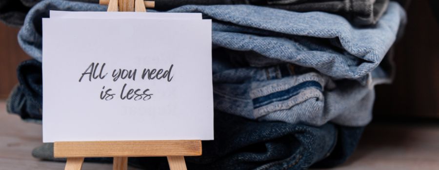 Pile of denim for repurposingwith a sign to say "All you need is less"