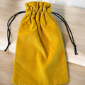 A handmade drawstring bag crafted from mustard yellow corduroy fabric, showcasing a soft textured appearance. The bag is cinched with black drawstring cords for a contrasting touch, combining functionality with bold color. It is displayed on a light wooden surface, highlighting the richness of the fabric.