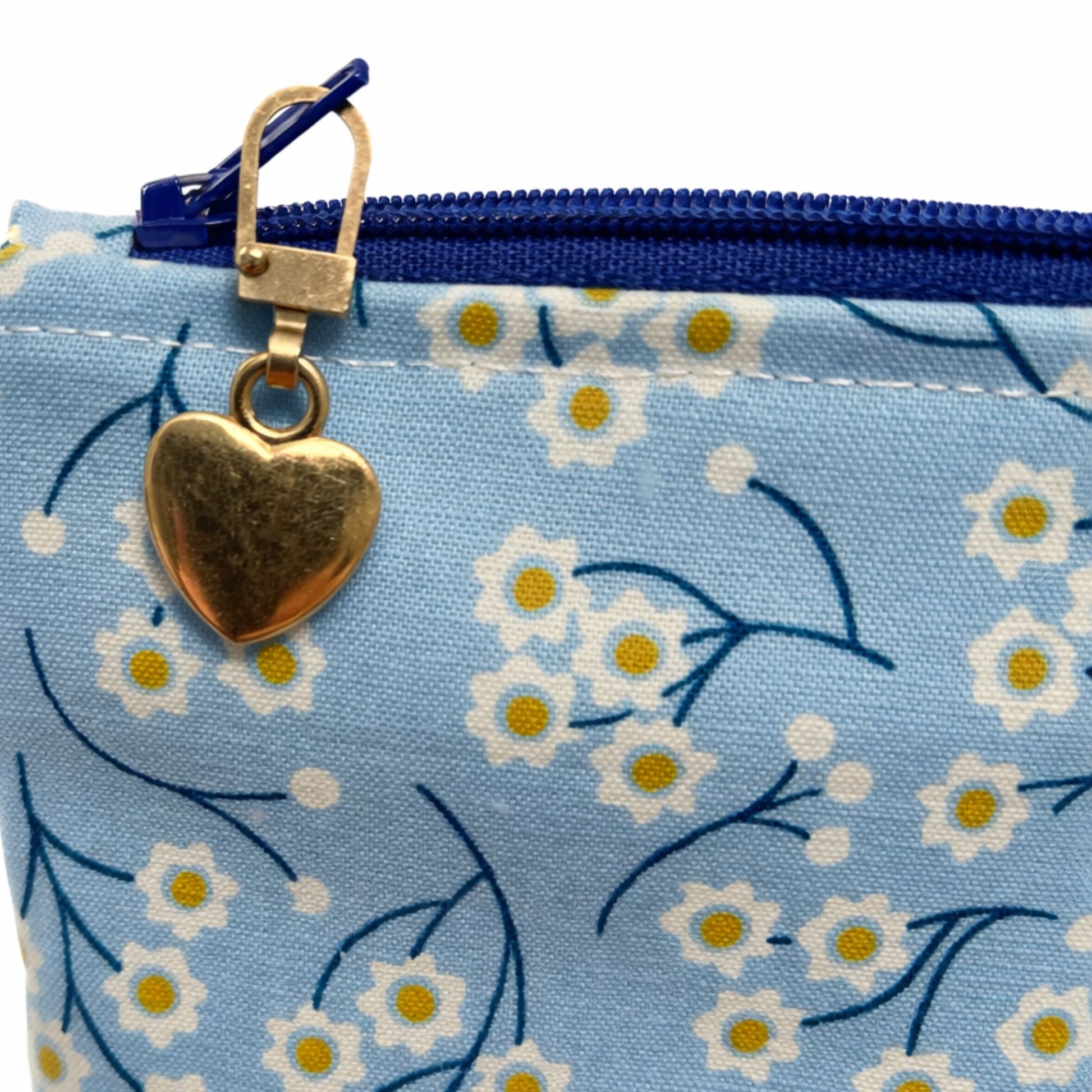 Blue pouch with floral pattern and gold heart charm on a white background
