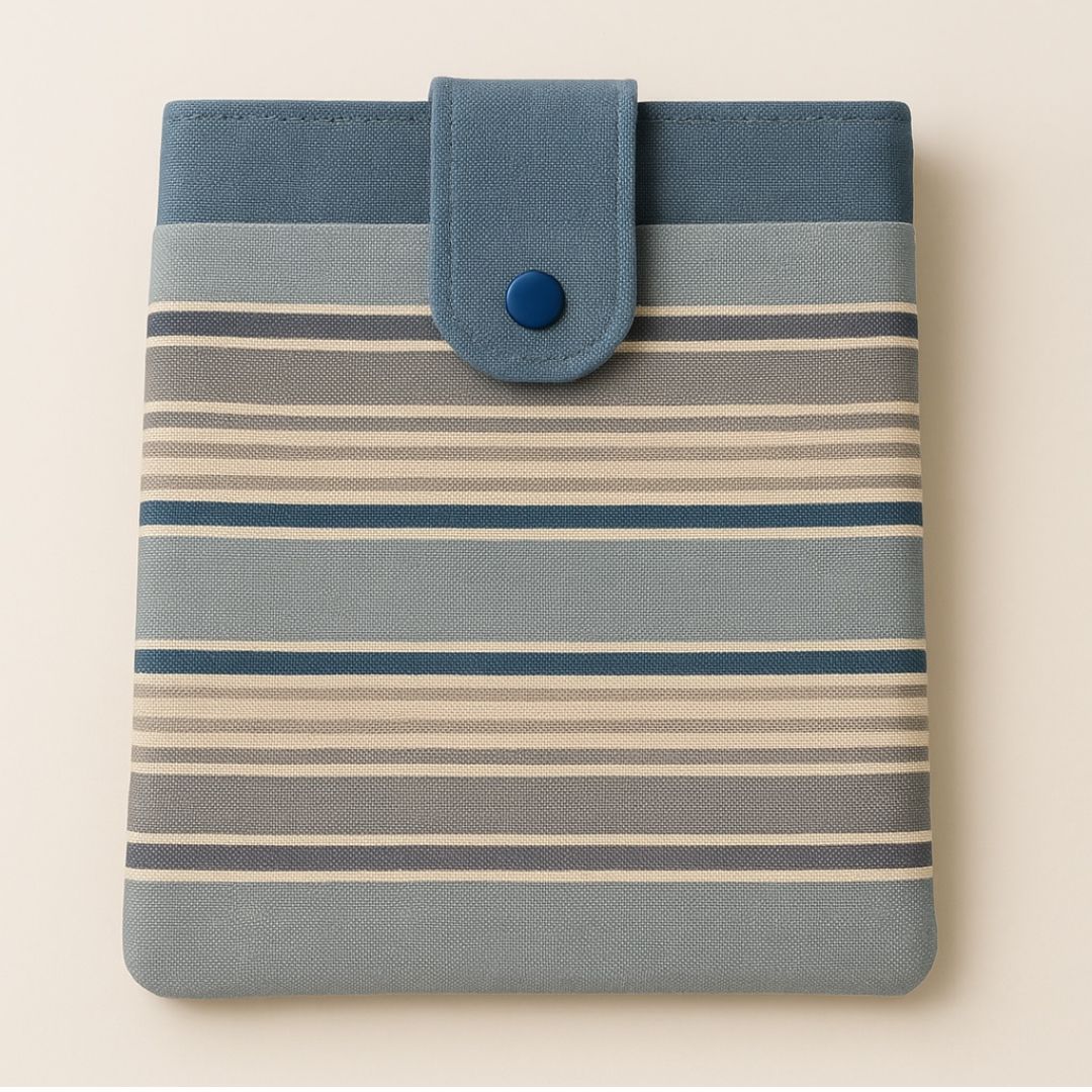 Striped tablet sleeve in blue, grey, and beige with snap closure and front pocket, photographed against a neutral background