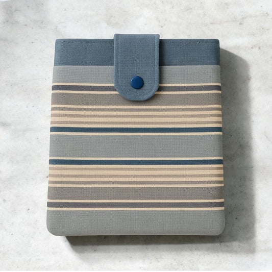 Striped tablet sleeve in blue, grey, and beige with snap closure and front pocket, displayed on a light marble surface