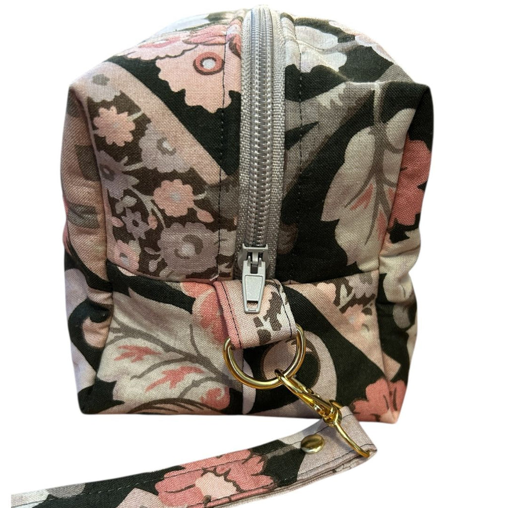 Close-up of a handmade brown floral makeup bag showing silver zip, boxed corner, and detachable wrist strap with gold swivel clasp.