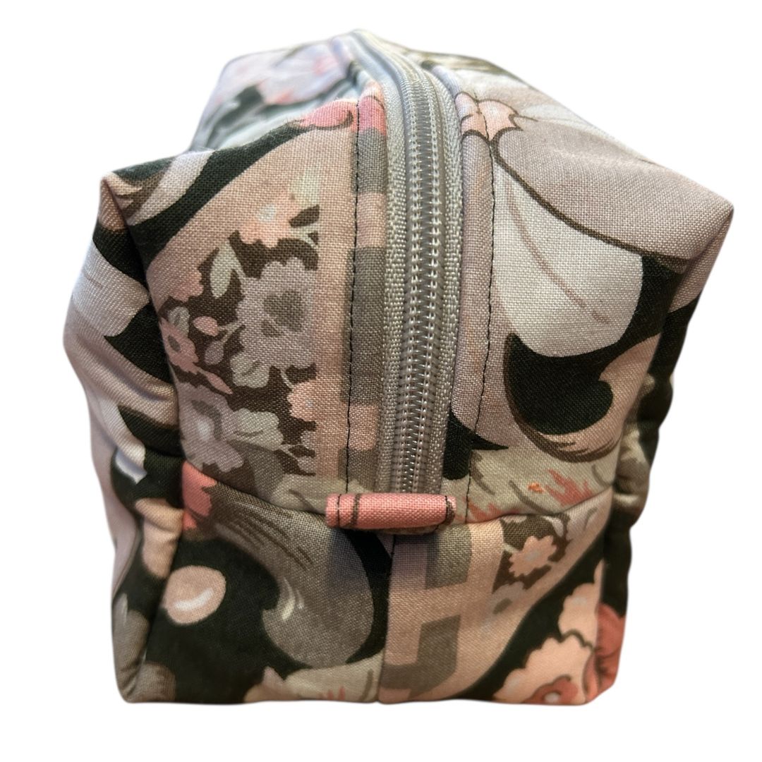 ide view of a handmade brown floral zip-up pouch showing the pink zip end tab and boxed corner detail.
