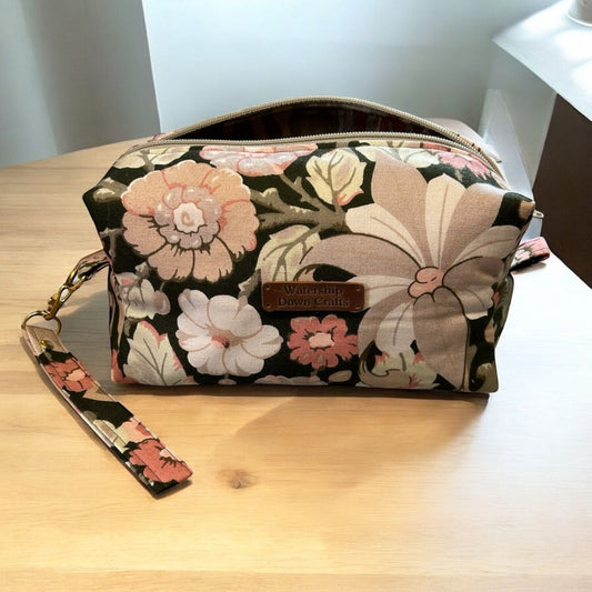 Handmade makeup bag in vintage brown floral fabric with soft pink and cream flowers, featuring a zip closure, detachable wrist strap, and Watership Down Crafts label.