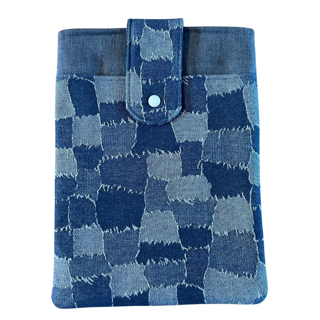 Front view of a denim patchwork print tablet sleeve with a blue snap-tab closure, photographed against a light background.
