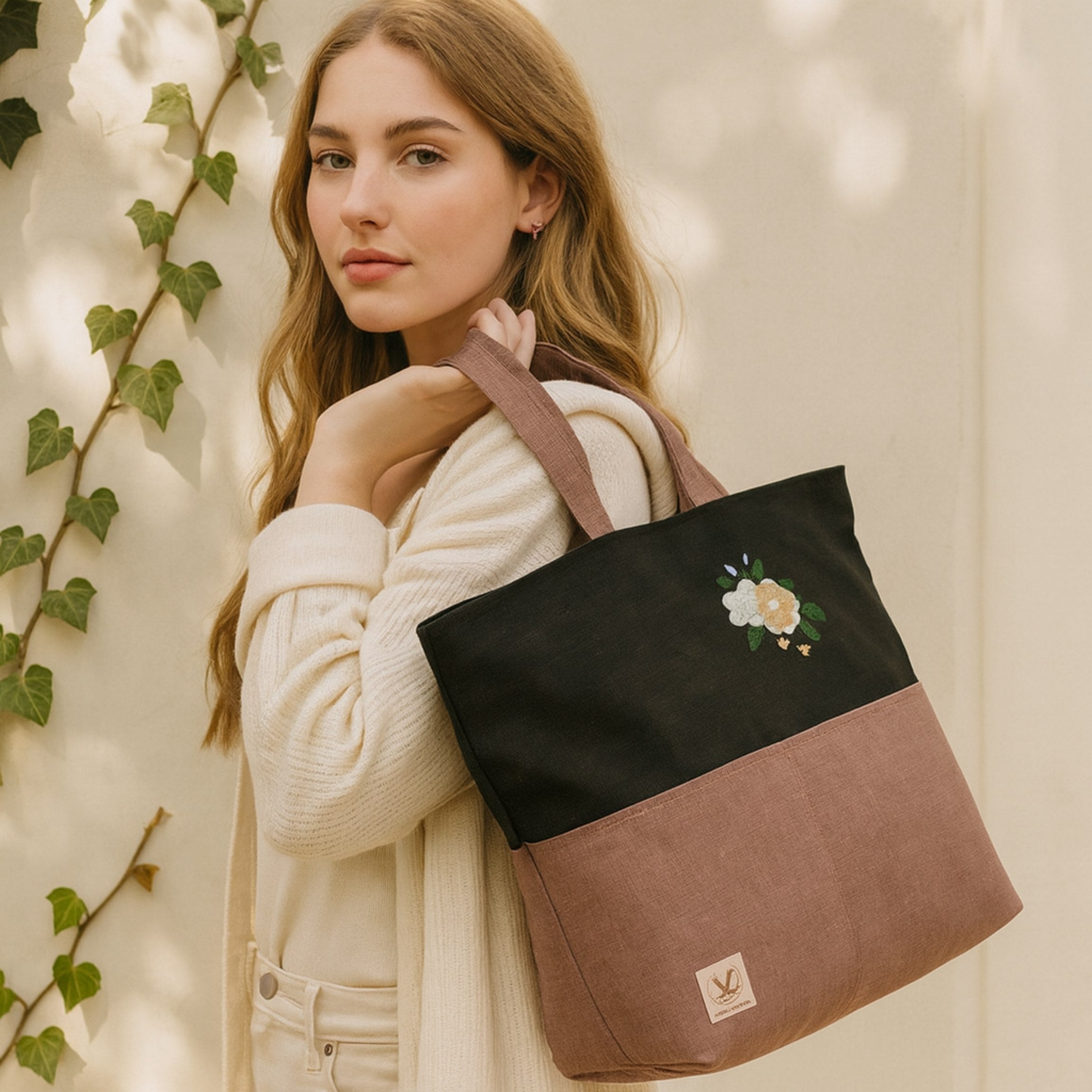 Woman holding a black and brown tote bag with floral design against a neutral background