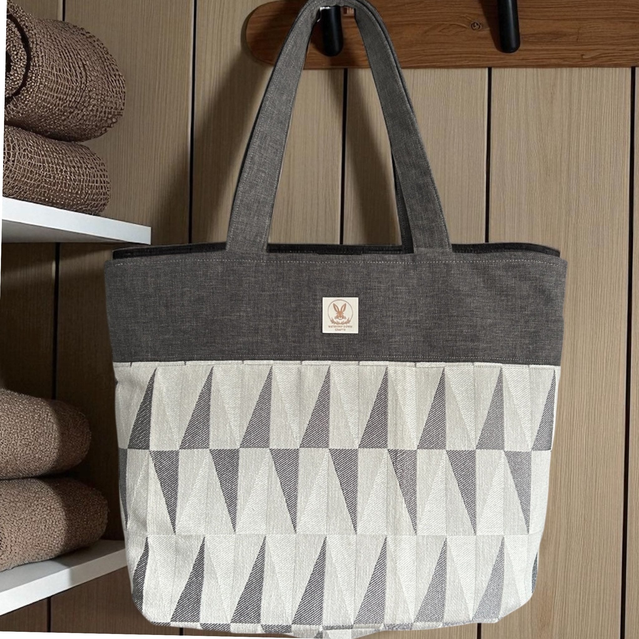 Gray and white geometric patterned tote bag with a brand logo on a wooden surface.
