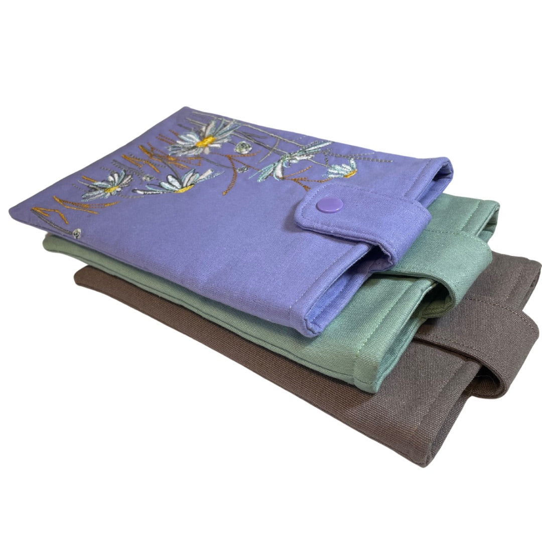 A collection of three Kindle sleeves in lilac, mint, and brown colors, each featuring an embroidered floral design on the front.