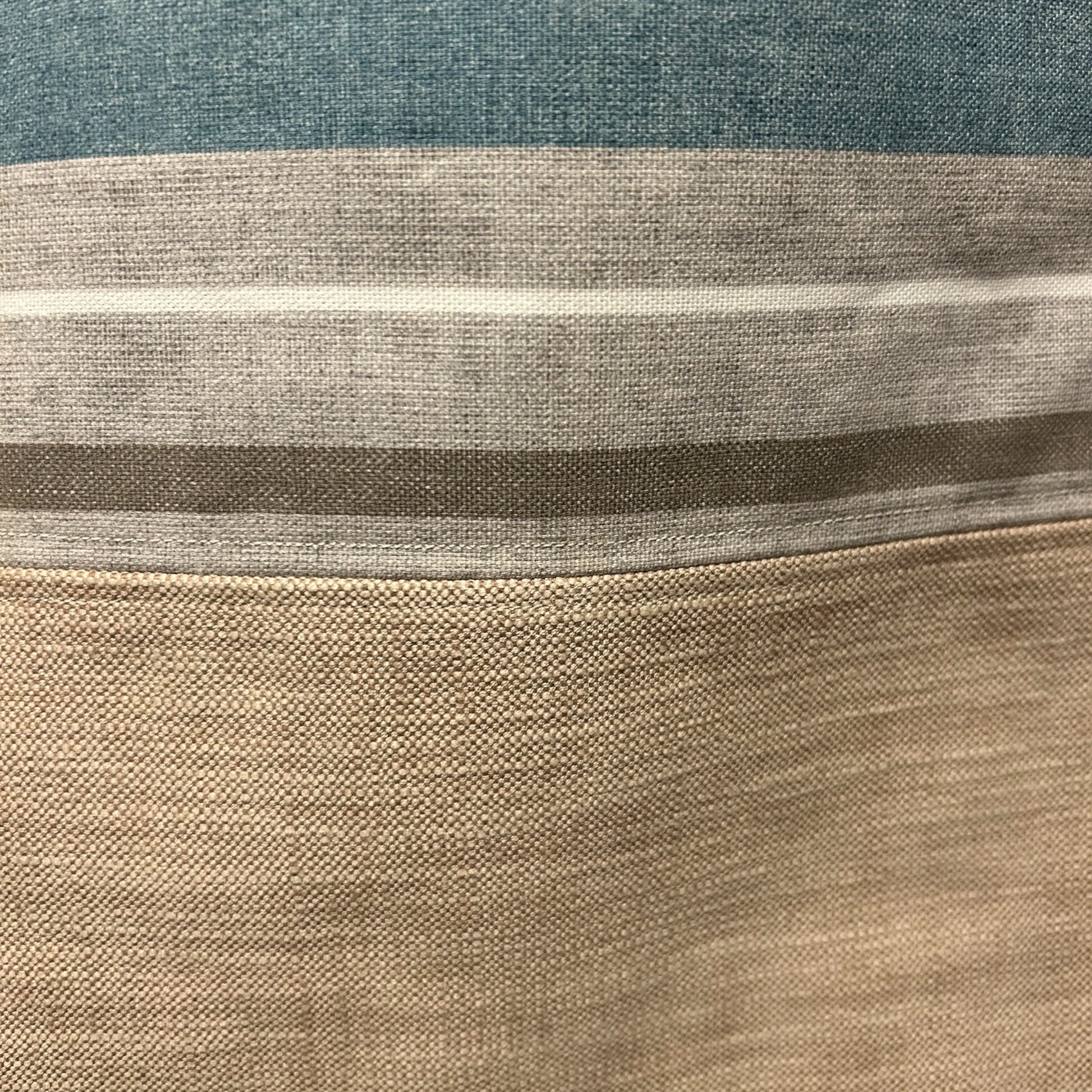 A close-up view of a tote bag's fabric, showcasing its textured material and horizontal stripes in shades of blue, beige, and gray. The detailed shot highlights the weave and color transitions, emphasizing the quality and subtle patterns of the fabric.
