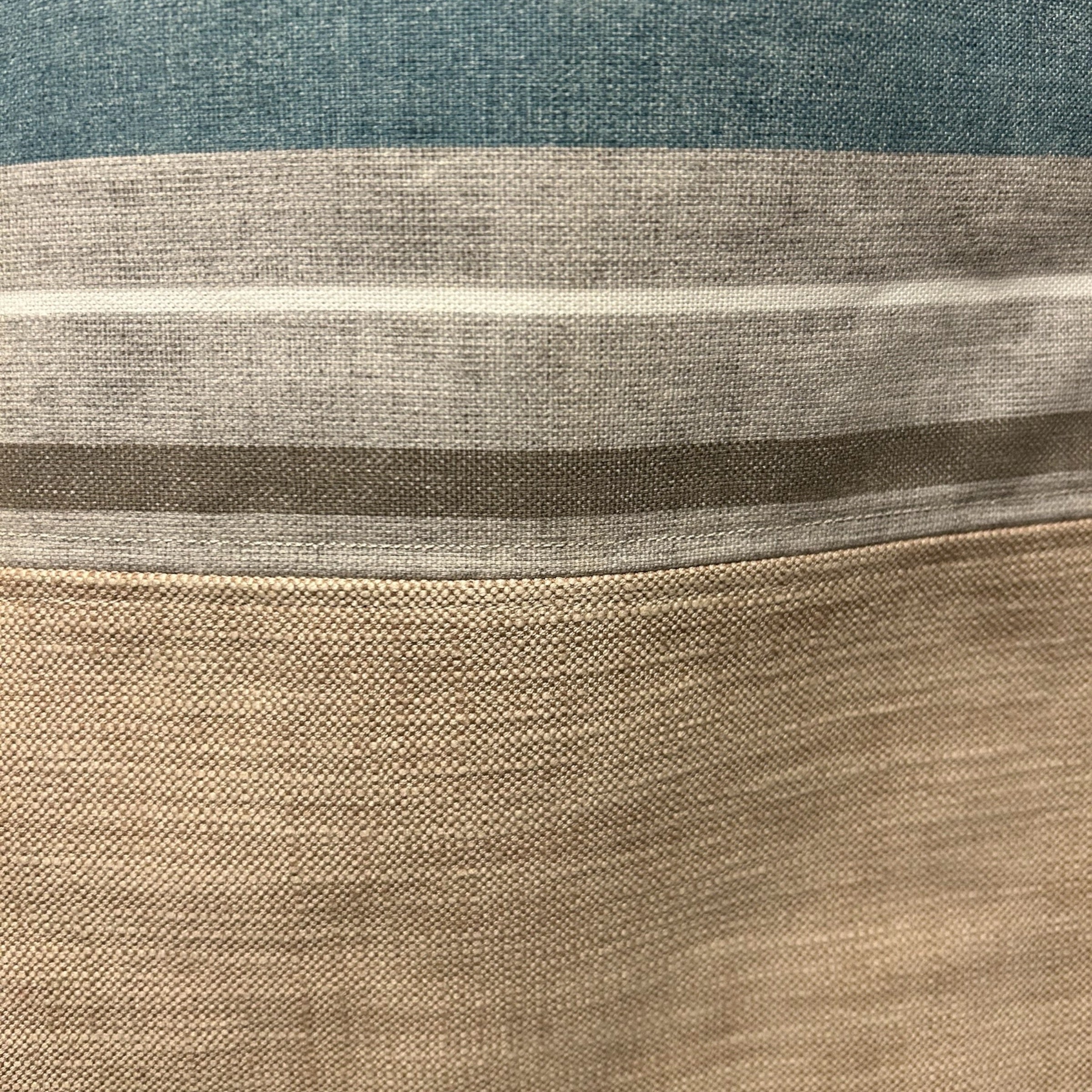 A close-up view of a tote bag's fabric, showcasing its textured material and horizontal stripes in shades of blue, beige, and gray. The detailed shot highlights the weave and color transitions, emphasizing the quality and subtle patterns of the fabric.
