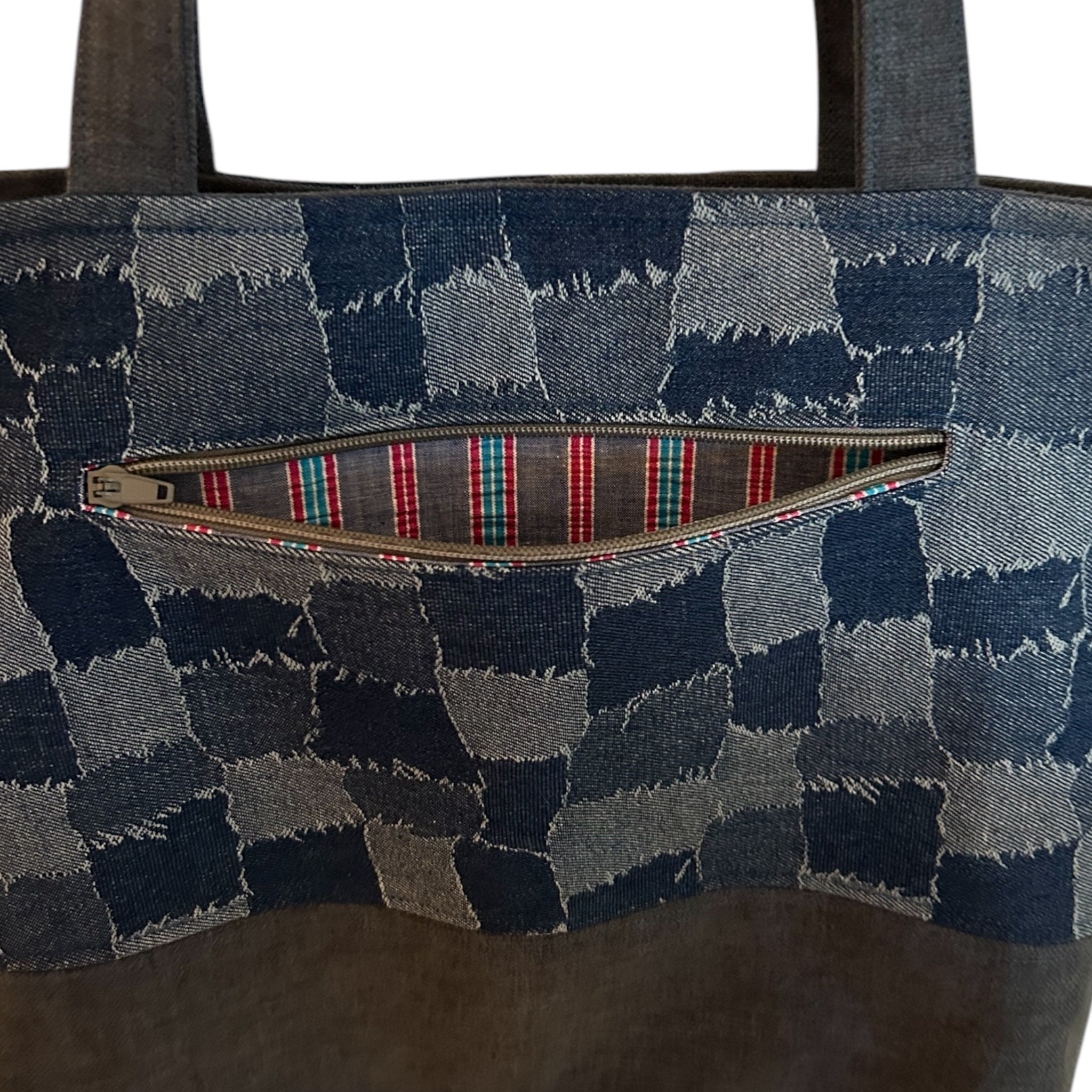 Close-up detail of a denim patchwork tote bag, showcasing an external zippered pocket with a vibrant striped lining. The checkerboard pattern adds a unique handmade touch, while the pocket provides convenient storage for small essentials.
