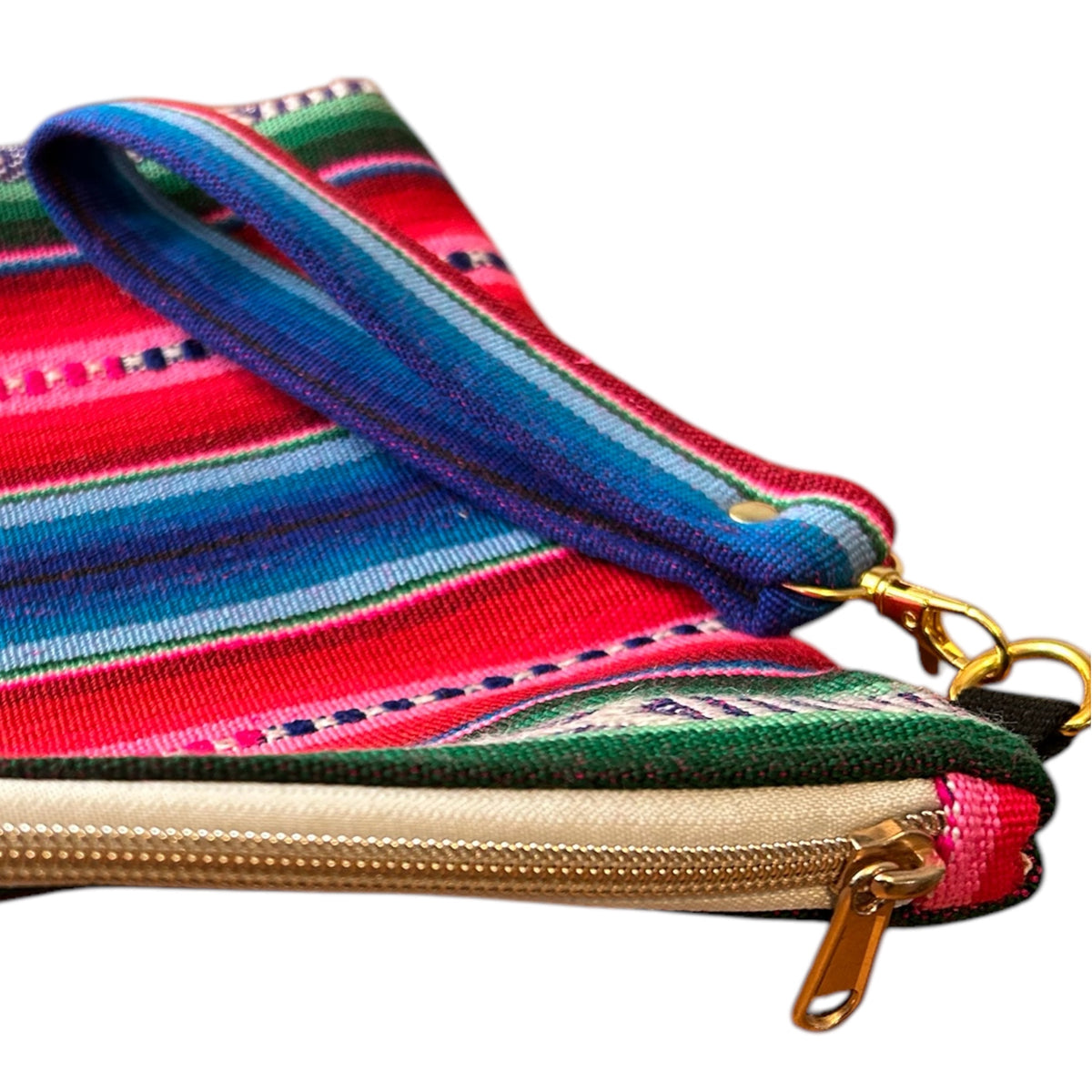 Close-up of a handmade zipper pouch featuring a vibrant pink, blue, and green woven fabric, a sturdy gold zipper, and a detachable wristlet strap with gold hardware. The intricate details highlight the craftsmanship and functional design.