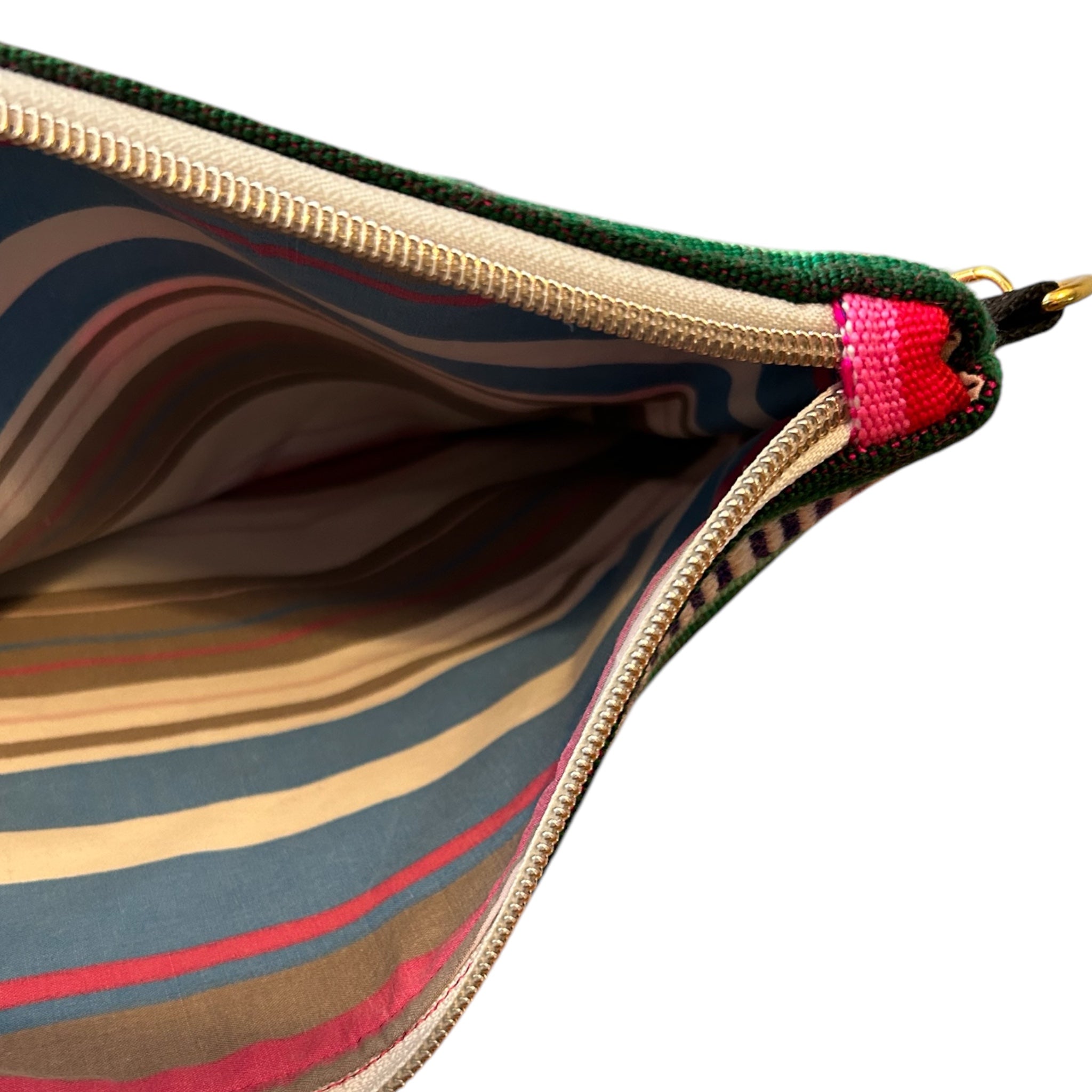 Close-up of the interior of a handmade zipper pouch featuring a vibrant striped cotton lining. The gold zipper and colorful woven fabric exterior complement the bold and practical design.