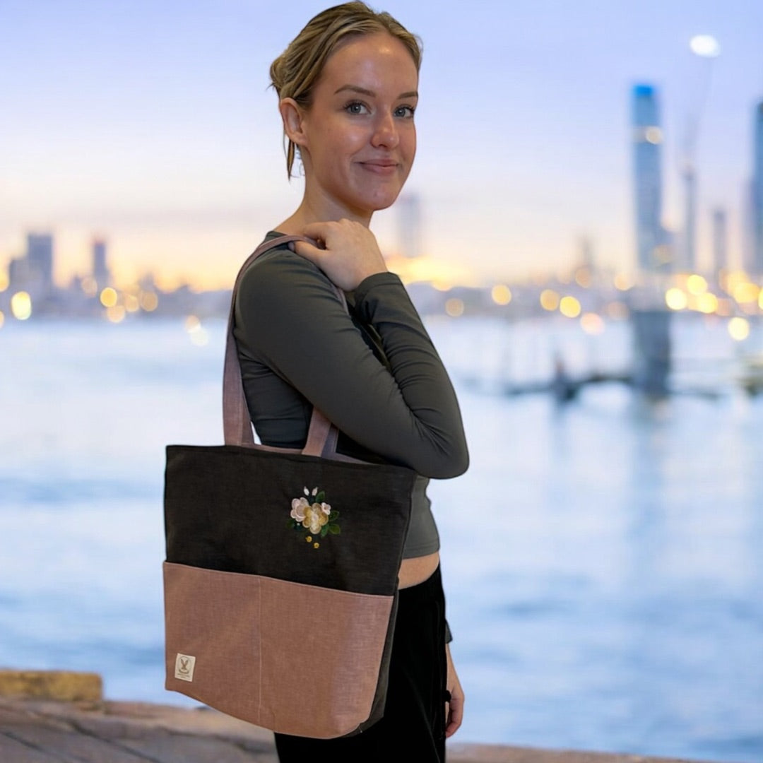 Woman by the waterfront at dusk, carrying a two-tone tote bag with floral embroidery.