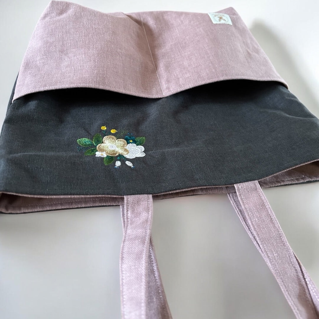 Flat-lay of a two-tone tote bag with floral embroidery and exterior pockets.