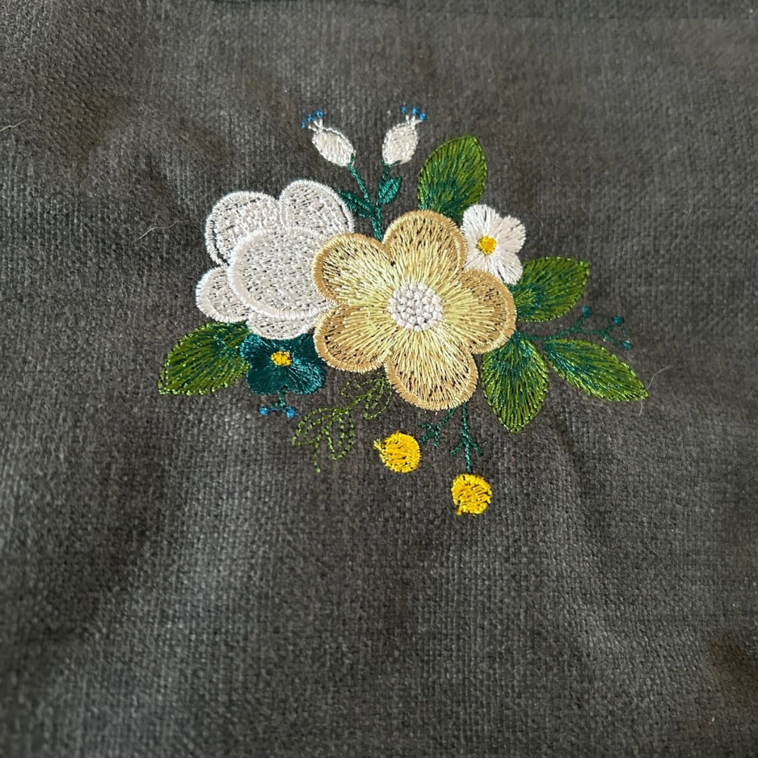 Close-up of floral embroidery on dark fabric, featuring yellow, white, and green details.