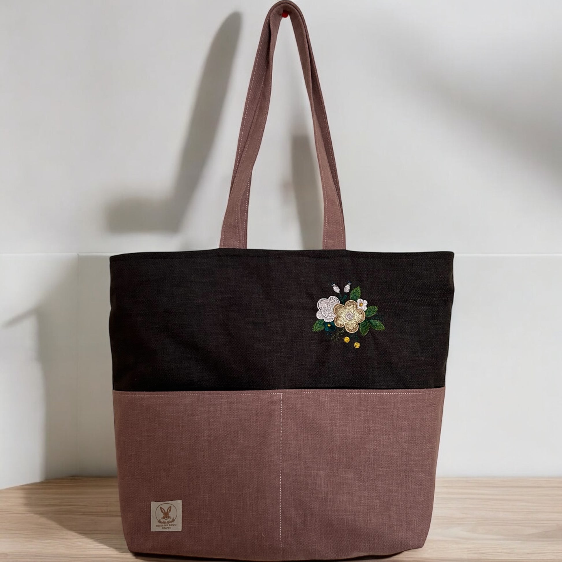 Two-tone tote bag with floral embroidery, standing upright on a wooden surface.