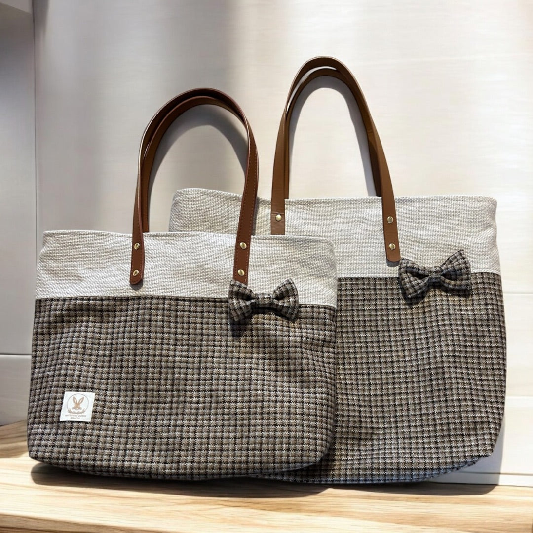 Two tweed tote bags with leather handles and decorative bows, displayed on a wooden surface.