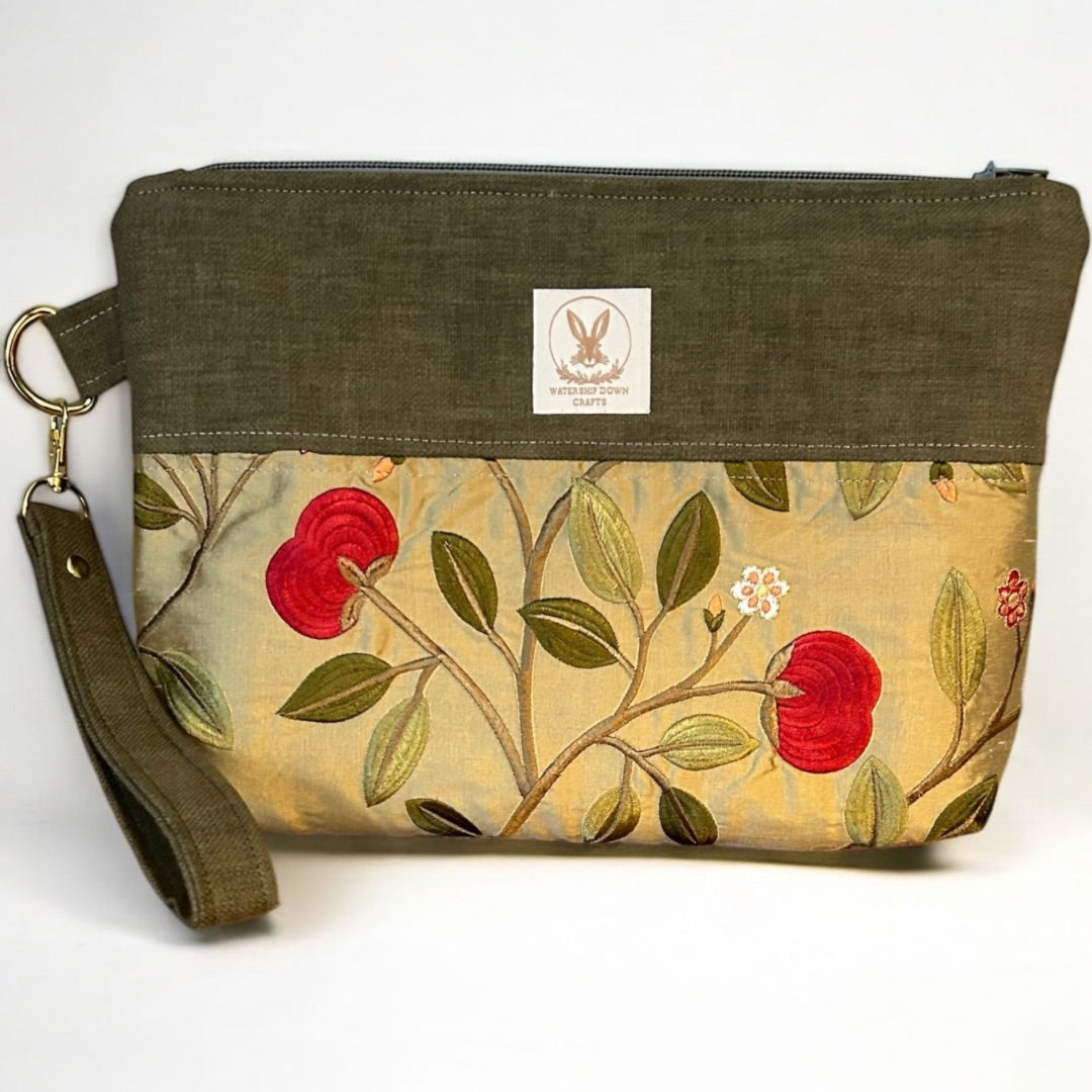 Handmade wristlet pouch in earthy olive green and gold, featuring a stunning floral embroidered design with bold red blooms. Crafted from rescued fabric offcuts, this eco-friendly clutch has a detachable strap, secure zipper closure, and gold-tone hardware, making it a stylish and sustainable choice for everyday use.