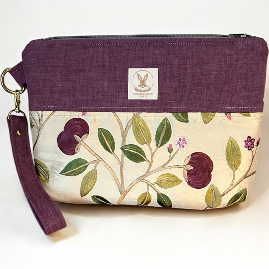 Handmade wristlet pouch in deep mulberry and cream, featuring a stunning floral embroidered design. Crafted from rescued fabric offcuts, this eco-friendly clutch has a detachable strap, secure zipper closure, and gold-tone hardware, making it both stylish and sustainable for everyday use.