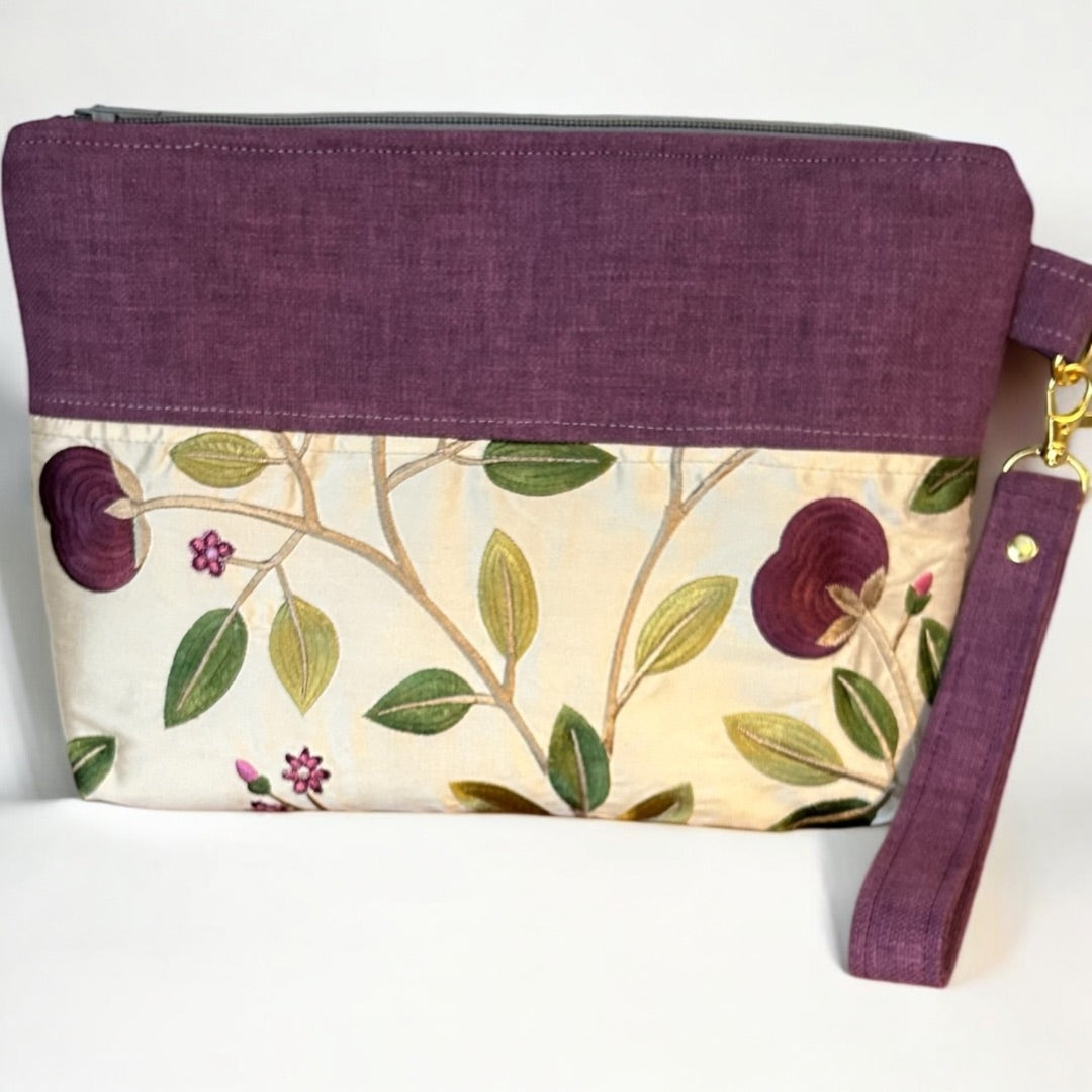 Handmade wristlet pouch in rich mulberry and cream, featuring a delicate floral embroidered design. Crafted from rescued fabric offcuts, this eco-friendly clutch has a detachable strap, secure zipper closure, and gold-tone hardware, making it a stylish and sustainable choice for everyday use.