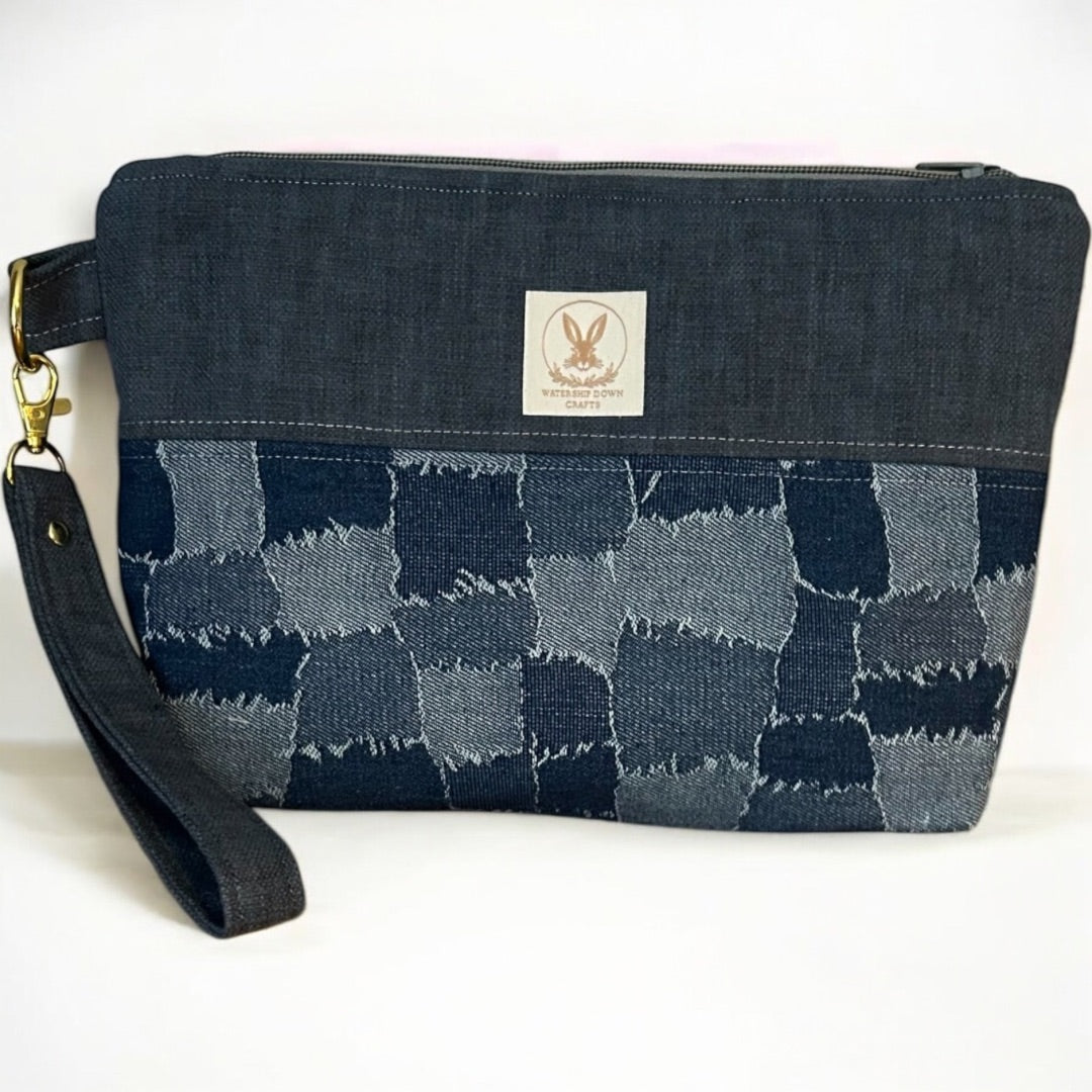 Handmade denim wristlet pouch featuring a patchwork-effect design in varying shades of blue. Crafted from upcycled fabric, this eco-friendly clutch has a detachable strap, secure zipper closure, and gold-tone hardware, making it a stylish and practical accessory for everyday use.